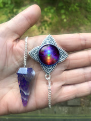 amethyst crystal pendulum featuring a rainbow chakra art pendant by Primal Painter. shown on a hand