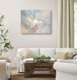 Very pale pastel peach, gray, and plum abstract angel canvas art with ethereal wings, sparkles, and a white starburst at the center hanging in a living room