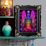 colorful chakra art print with a fuchsia angel torso with the seven chakra colors aligned down the center, and blue lights in her hands and a Reiki symbol over her head, in a black frame on a shelf