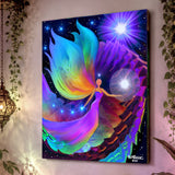 The Divine Path by Primal Painter is a stretched canvas print featuring an angel holding a white orb, huge rainbow wings and dress, blue orbs in one hand, moving up spiraling rainbow steps toward a violet light source. Hanging on a mauve wall