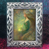 Framed artwork of a woman with long hair and a glowing orb, against a dark, textured background.