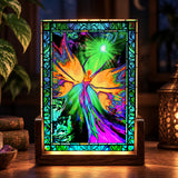 A colorful stained-glass-style decorative panel on a wooden stand, featuring a glowing fairy with bright green, blue, purple, orange, and pink tones, displayed on a table with plants and a lantern in a dim interior setting.