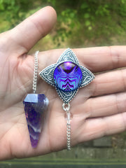 An amethyst crystal with a silver pendant featuring blue and purple geometric artwork by Primal Painter