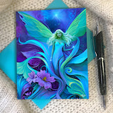 Greeting card with an ethereal blue fairy emerging from purple flowers by Primal Painter on a textured surface with a pen.