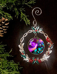 A metal Christmas ornament featuring a round, sparkly frame with 'guardian angel' artwork by Primal Painter, surrounded by green holly and a red cardinal.