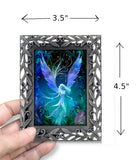 Framed artwork of a fairy with blue wings held by a hand, showing dimensions.