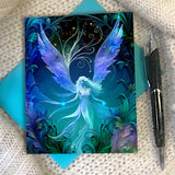 Greeting card with a fairy design featuring blue and green wings on a textured surface.
