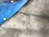 Close-up of gray fabric with a blue blanket showing the whipstitch border partially visible
