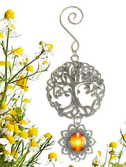 A pewter Tree of Life ornament with a hanging flower-shaped pendant featuring a 'Light Being' artwork by Primal Painter, displayed against a background of yellow flowers.