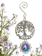 A pewter Tree of Life ornament with a purple angel artwork pendant below it by Primal Painter, against a background of flowers.