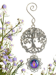 A pewter Tree of Life hanging ornament with a violet flame art pendant, displayed against a background of purple flowers. Art by Primal Painter