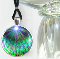 A necklace featuring a vibrant, abstract print of green and blue chakra rays on a round pendant, set in a silver or brass setting with a black suede faux leather cord and an art deco-style hook and eye clasp by Primal Painter.