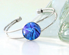 A silver colored wire bracelet with  blue artwork of a goddess sealed under a round glass dome by Primal Painter