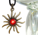bronze sun shaped necklace with an embellished bail and featuring bright red starburst artwork representing the root chakra and set under a glass dome