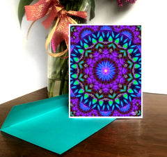 A greeting card with a colorful mandala design featuring purple, blue, and green, with a white border and a matte finish on the inside for writing.