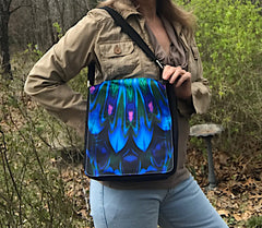 A person carrying a black messenger bag with a blue and green abstract art flap, featuring a snap-on closure. Art by Primal Painter